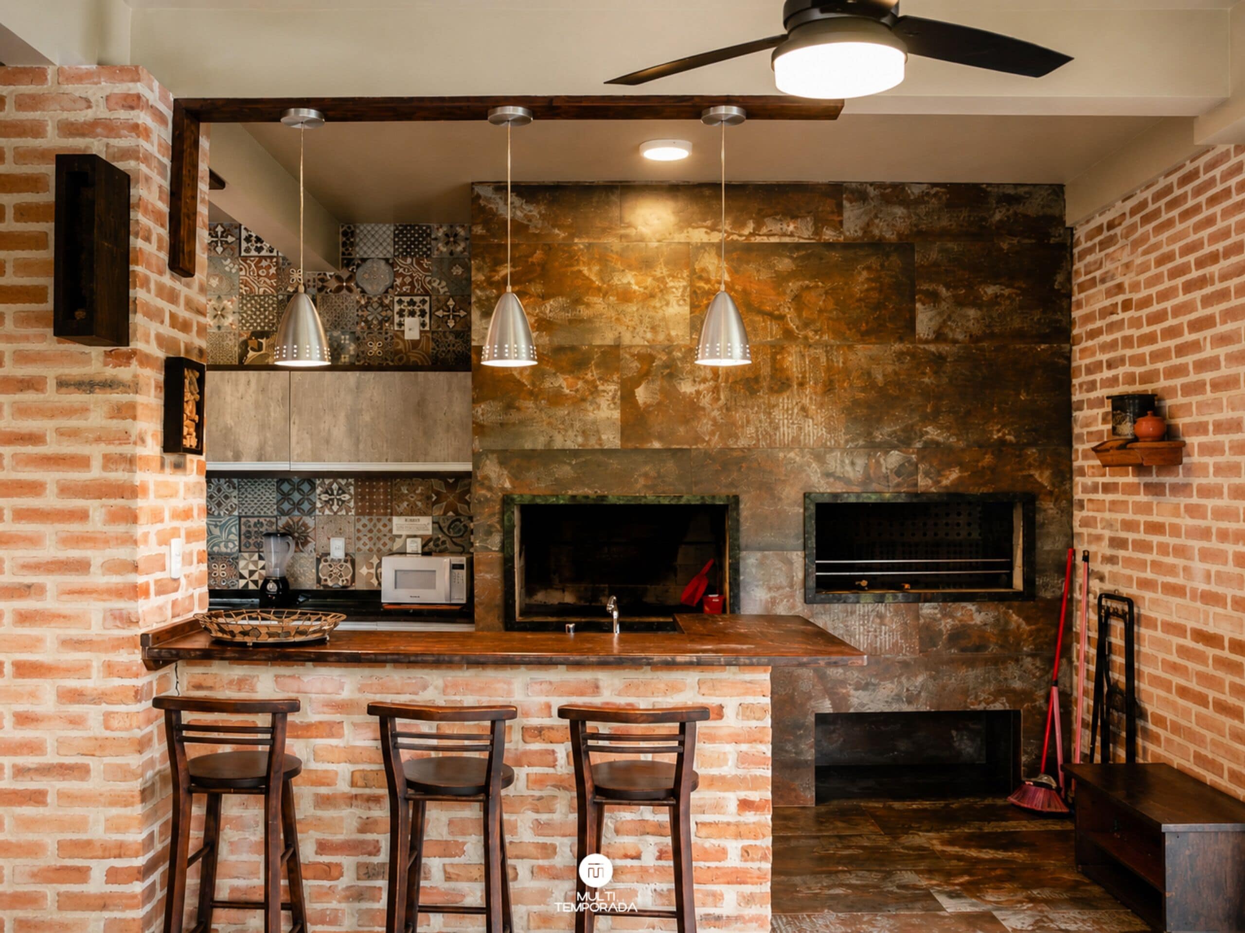 Una cocina con pared de ladrillo, microondas, pileta y barra con taburetes.