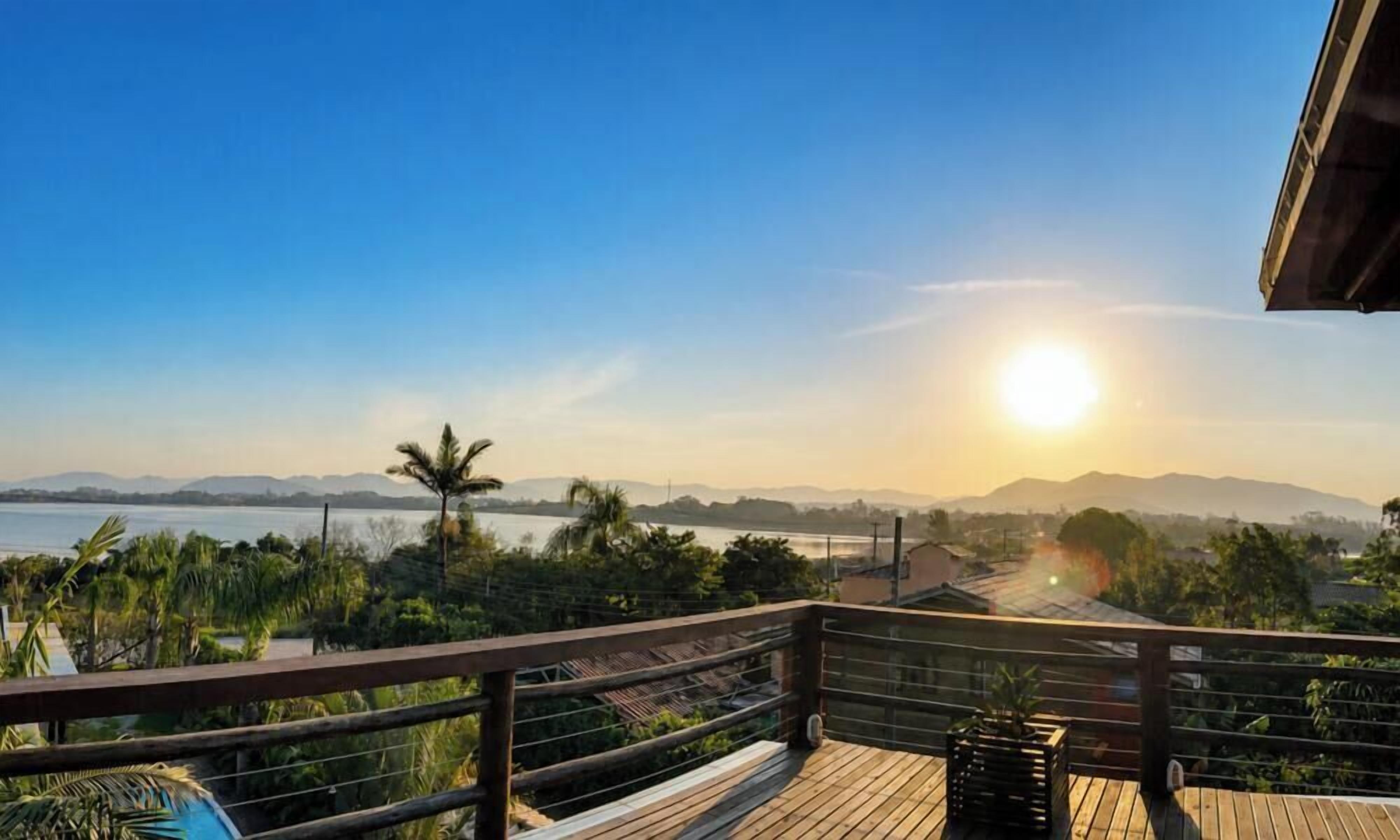 Um deck de madeira com vista para um corpo d'água e montanhas distantes ao pôr do sol.