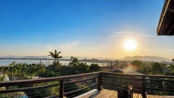 Um deck de madeira com vista para um corpo d'água e montanhas distantes ao pôr do sol.