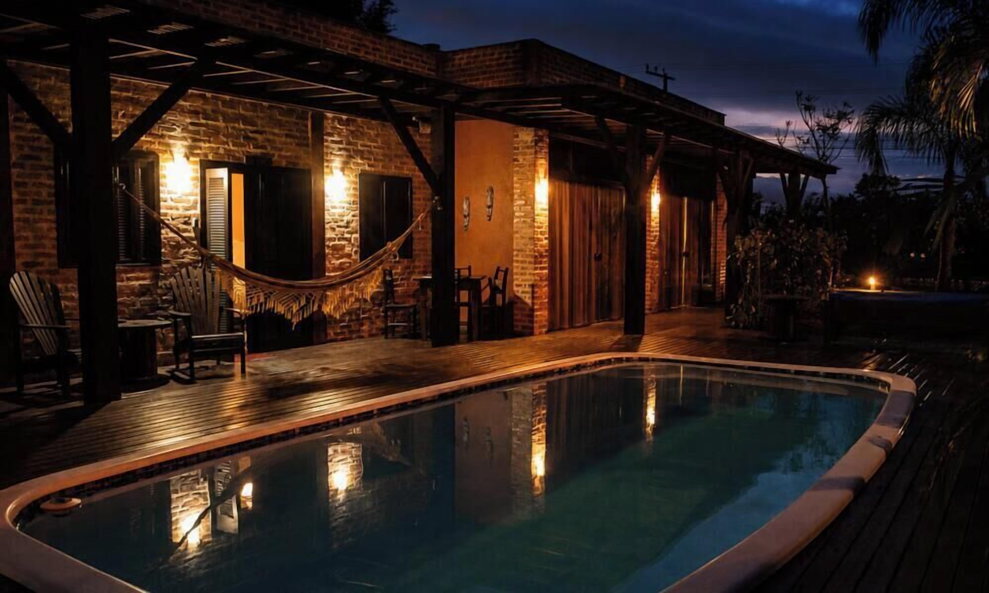 A pool area with a wooden deck, a hammock, and a brick building with a covered patio.