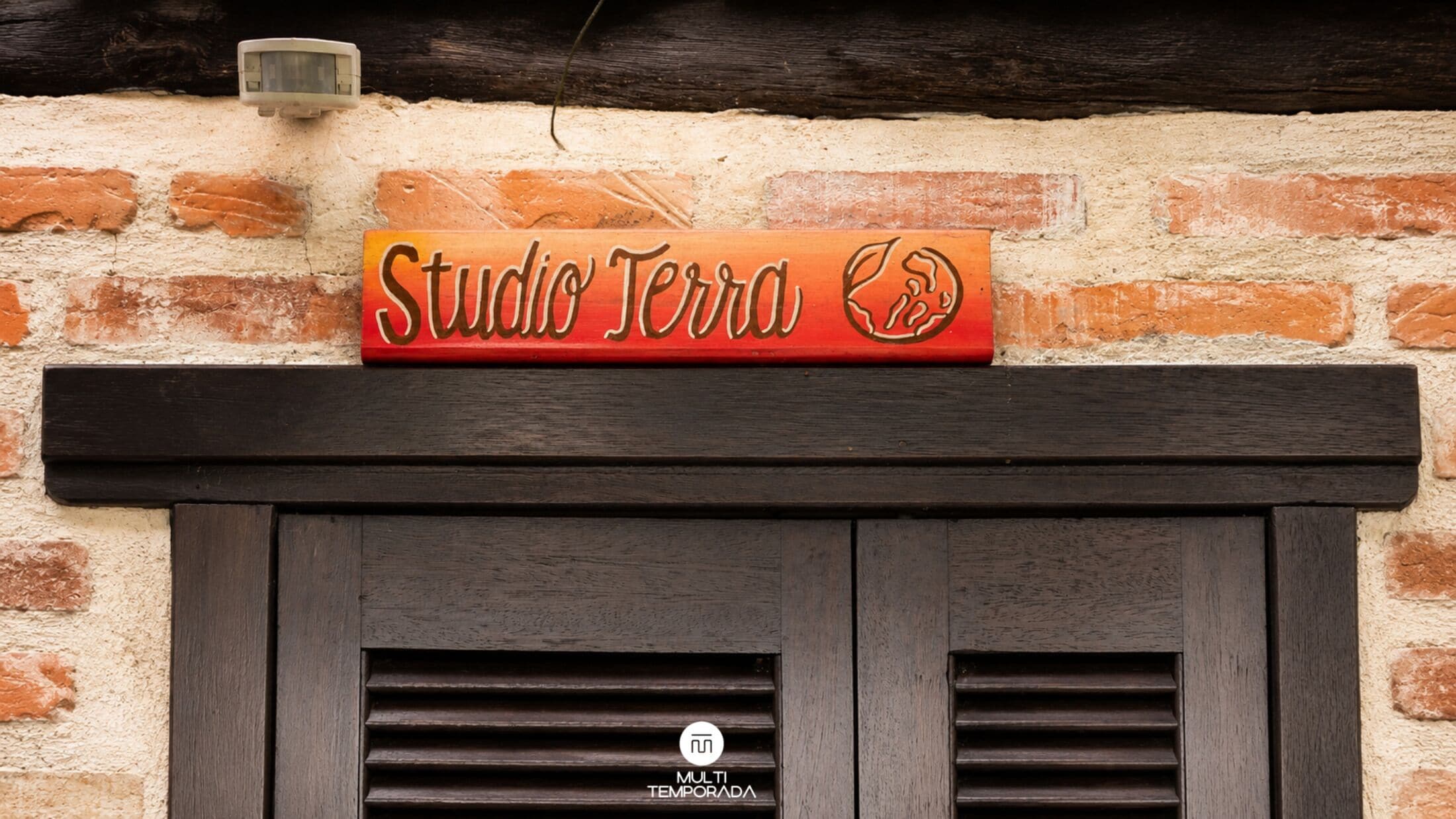 Un muro de ladrillo con un letrero que dice 'Studio Terra' y una puerta de madera oscura con un ventanal.