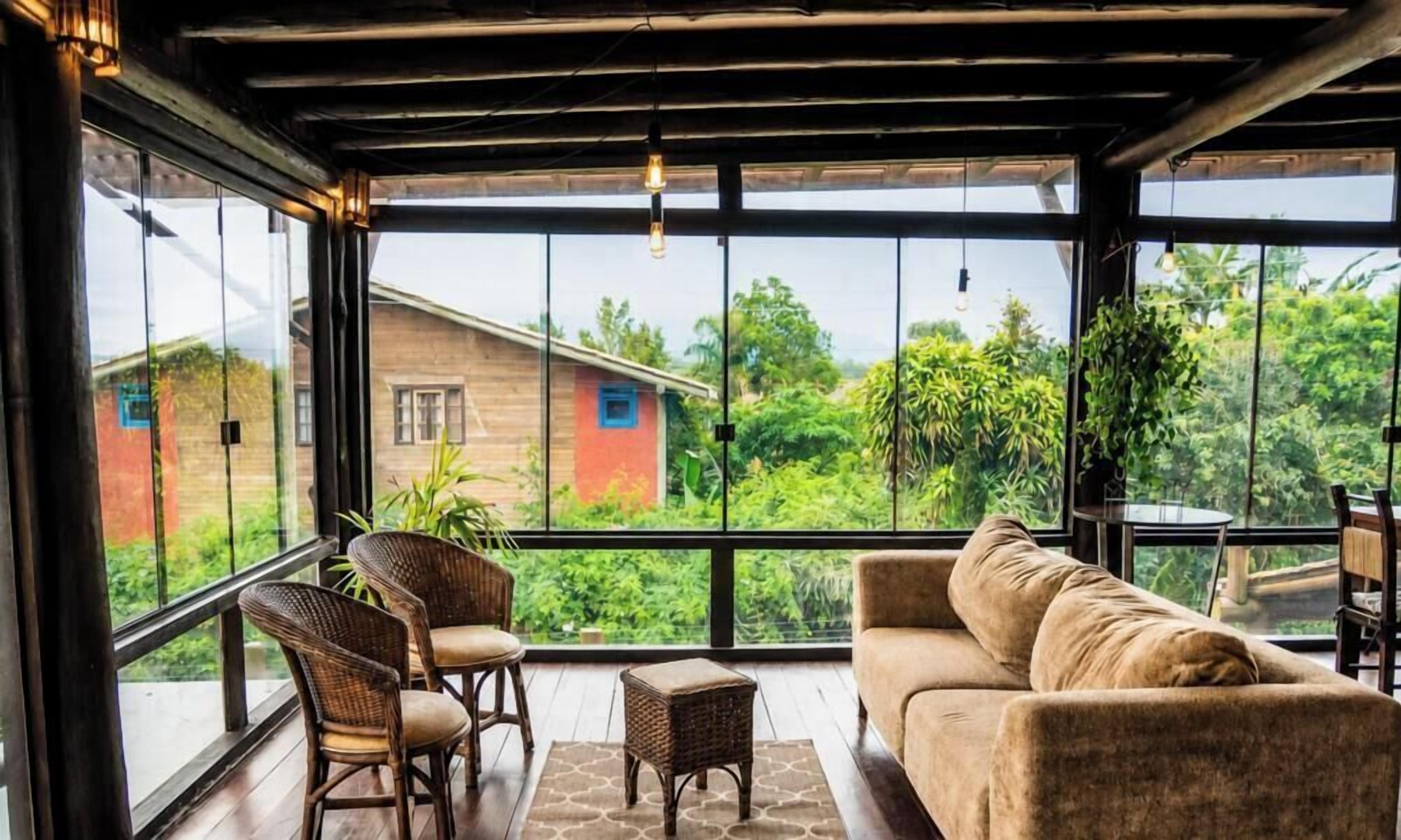 A room with a large window, wicker furniture, and a view of greenery and a building outside.