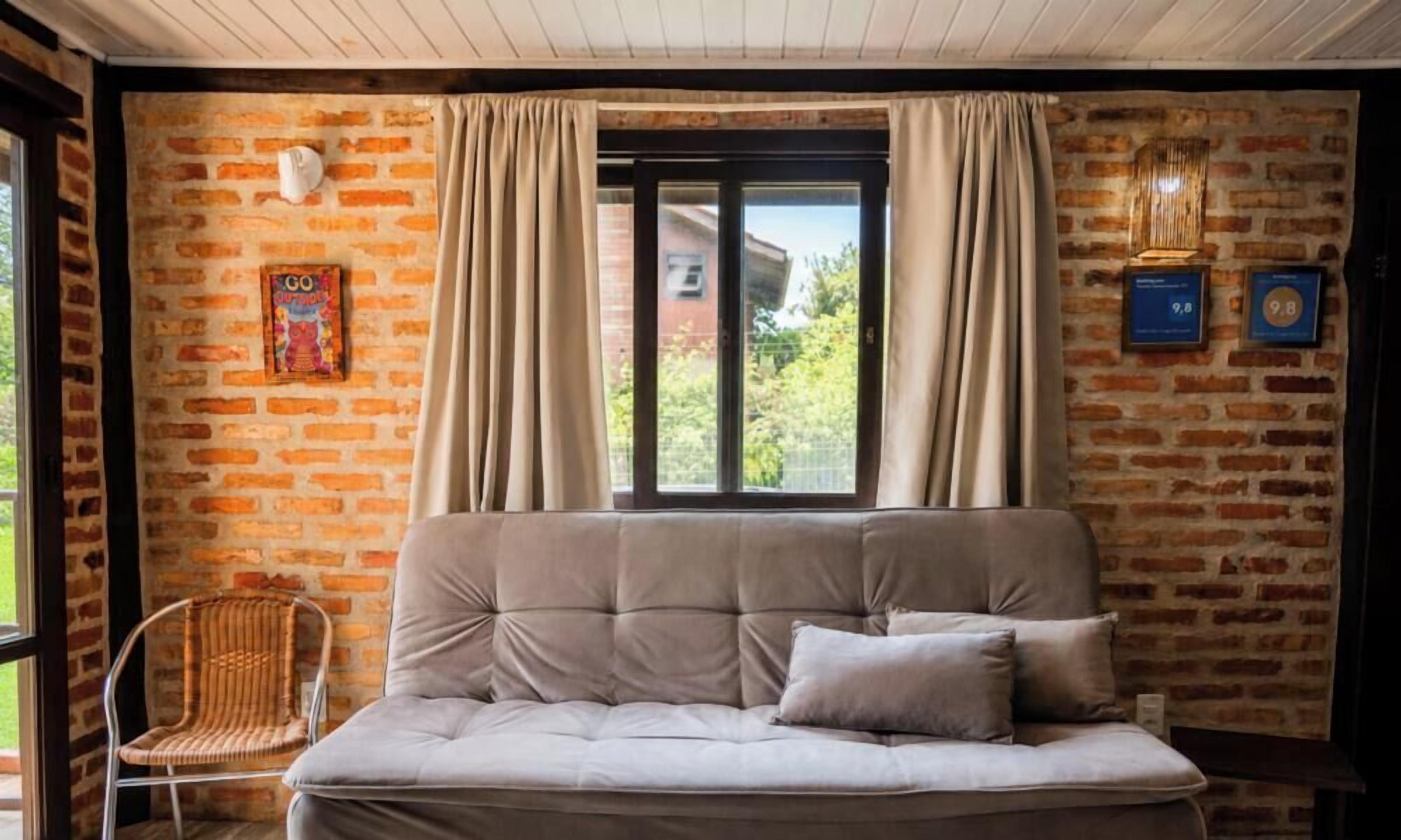 A room with a brick wall, a sofa, a chair, and a window with curtains.