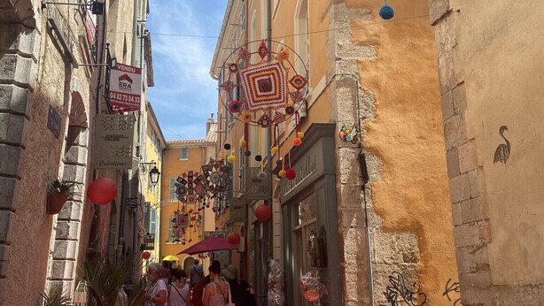 Eine schmale Straße mit Gebäuden an beiden Seiten, verziert mit bunten hängenden Ornamenten und einem roten Teppich.