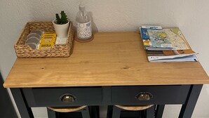 Ein Holztisch mit zwei schwarzen Schubladen und einem Korbkörbchen, das einen Blumentopf, eine Handdesinfektionsflasche und ein Taschentuchpaket enthält.