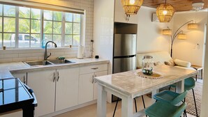 A modern kitchen with white cabinets, a stainless steel refrigerator, a sink, and a dining area with a table and chairs. - Newly renovated cottage steps from the water (Bimini)