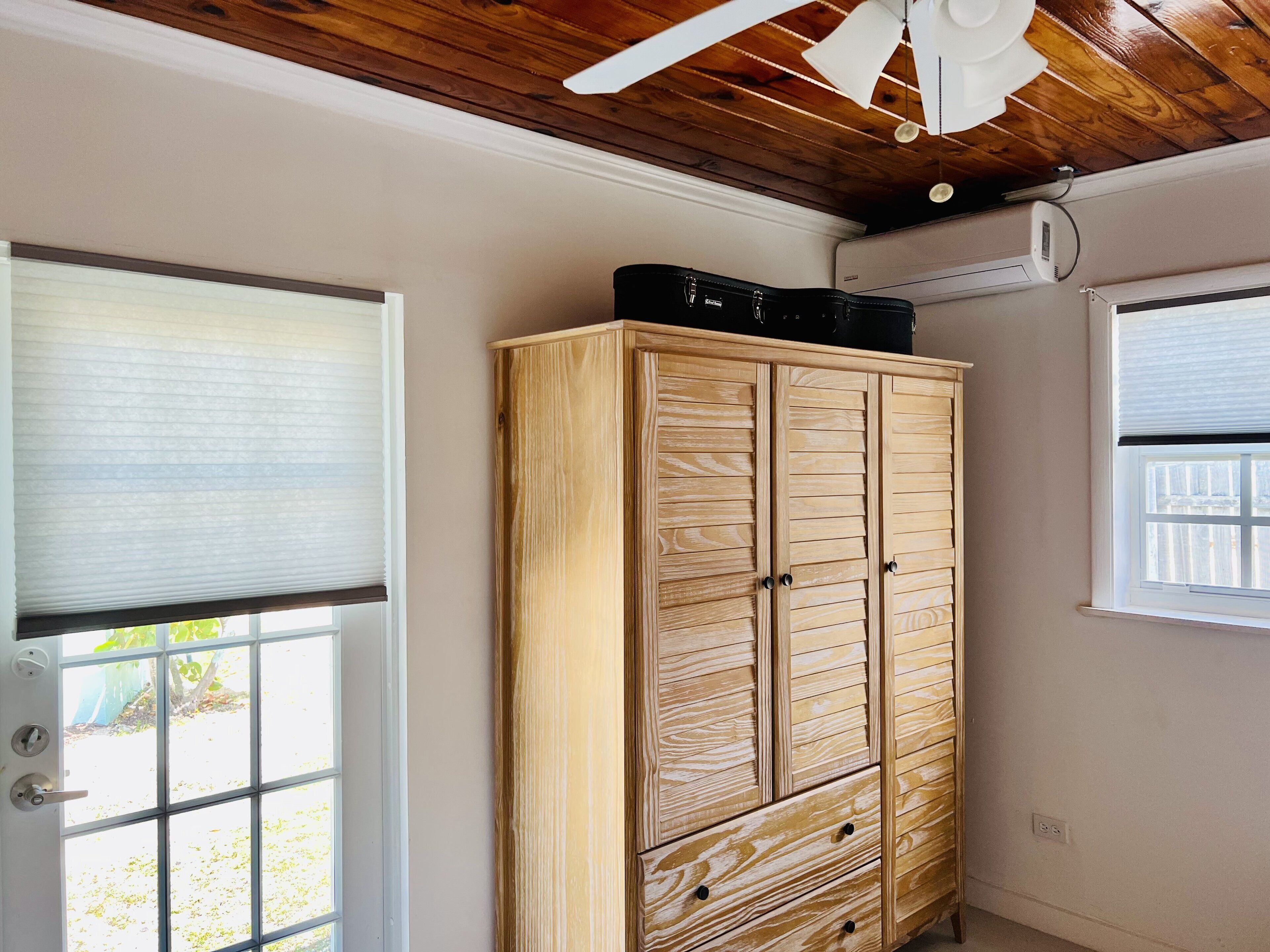 A room with a wooden wardrobe, a ceiling fan, and an air conditioning unit.
