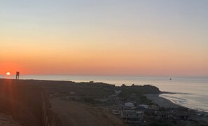 Eine Küstenlandschaft mit Sonnenuntergang, Strand und einer kleinen Siedlung mit Gebäuden.