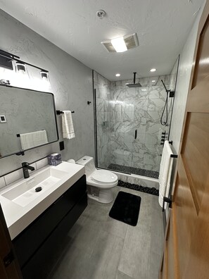 A modern bathroom with a large mirror, white sink, and a glass-enclosed shower area.