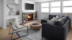Ein modernes Wohnzimmer mit Kamin aus Stein, einem grauen Sofa, einem Holztisch und einem an der Wand befestigten Fernseher.