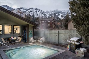A pool area with a view of snow-covered mountains, a barbecue grill, and outdoor seating.