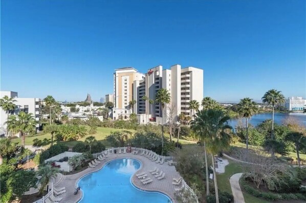 Relax by the oval-shaped pool surrounded by lounge chairs and palm trees, with a view of the nearby water.