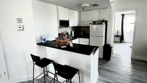 A modern kitchen with white cabinets, a black countertop, and two black bar stools. - Universal/Pool view +FREE parking. Newly renovated 2bdrm/2bth (Orlando)