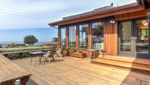 Um deck de madeira com móveis para área externa, janelas amplas e vista para o oceano.