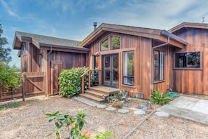 A modern wooden house with a front porch, large windows, and a well-maintained garden.