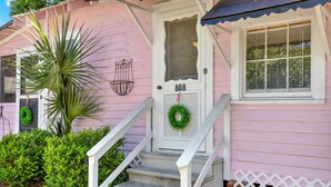 Una casa rosa con puerta blanca marcada "808", un porche con escalones, una planta en maceta y un pequeño jardín.