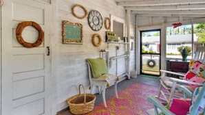 Una habitación con paredes de madera blanca, una cesta de mimbre, una silla verde y una alfombra colorida.
