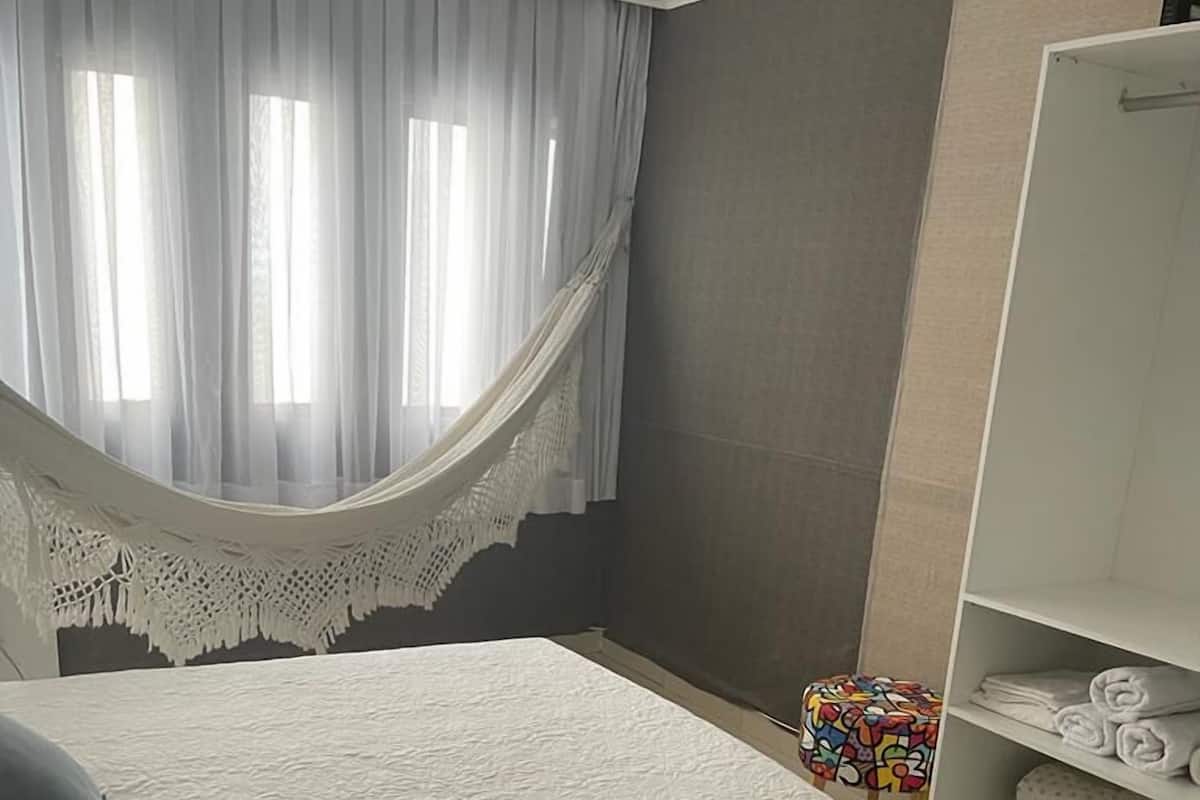 A bedroom with a bed, a white wardrobe, a colorful stool, and a patterned rug.
