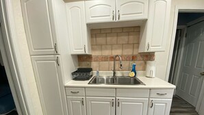 Una cocina con armarios blancos, un lavamanos de acero inoxidable y un salpicadero de azulejos.