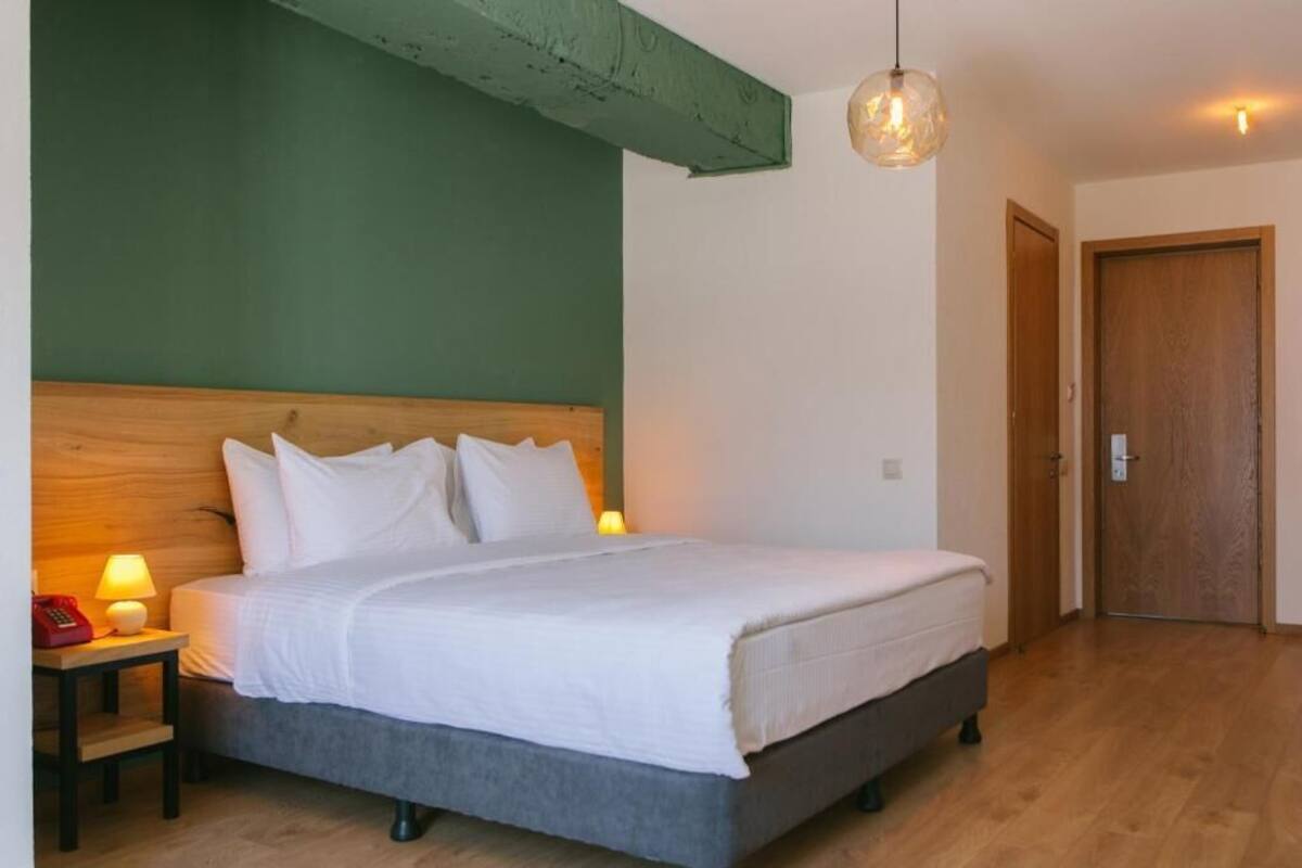 A bedroom with a wooden headboard, a bed with white bedding, a bedside lamp, a telephone, and a wooden door.
