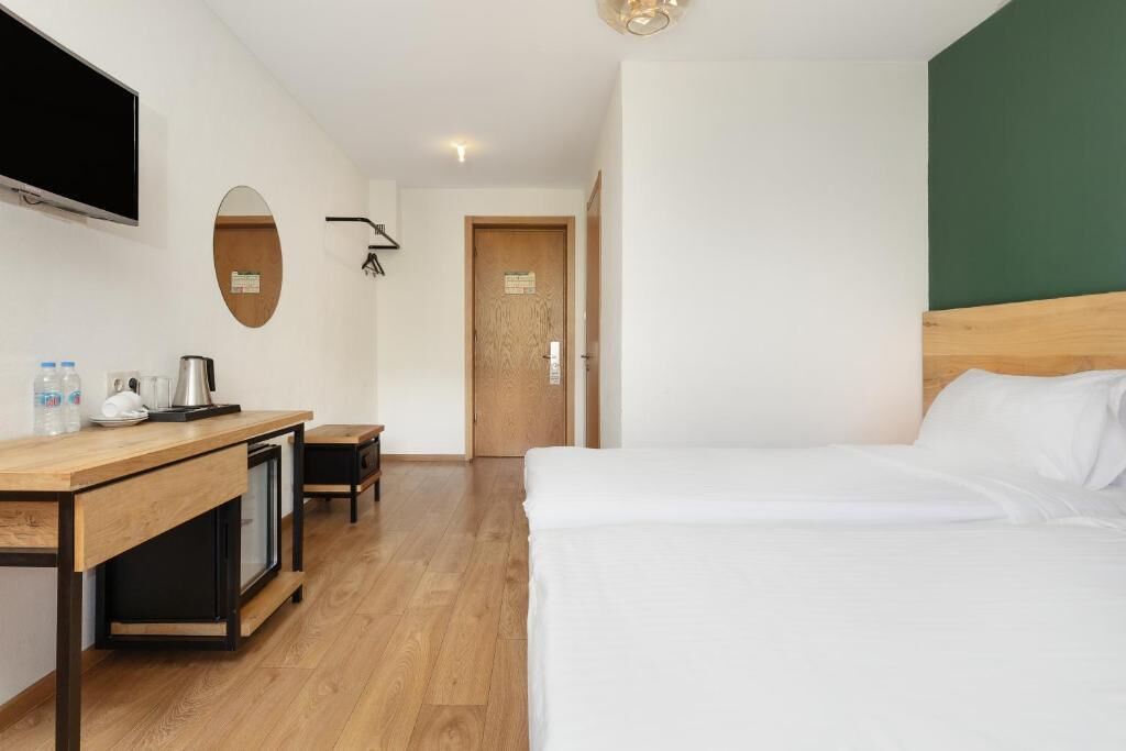 Una habitación de hotel con cama, escritorio con televisor, cafetera y espejo.