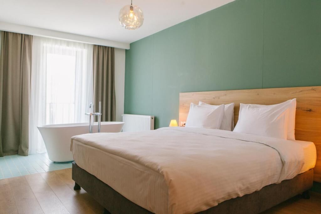 A bedroom with a large bed, a wooden headboard, a bathtub, and a window with curtains.
