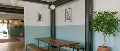 A wooden table with benches in a room with light blue walls, a large potted plant, and artwork on the walls.