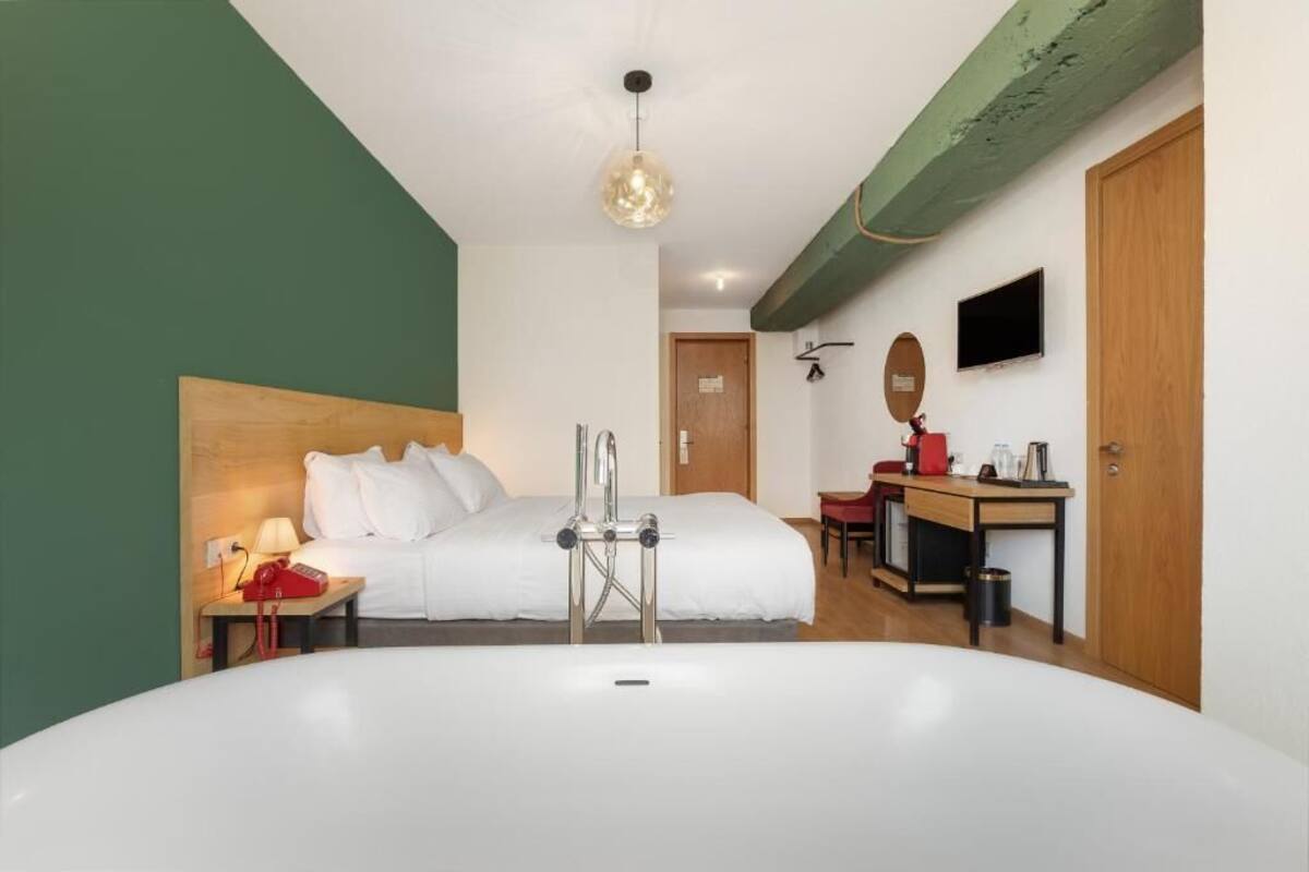 A modern hotel room with a large bed, a desk with a computer, a TV, and a bathroom with a bathtub.