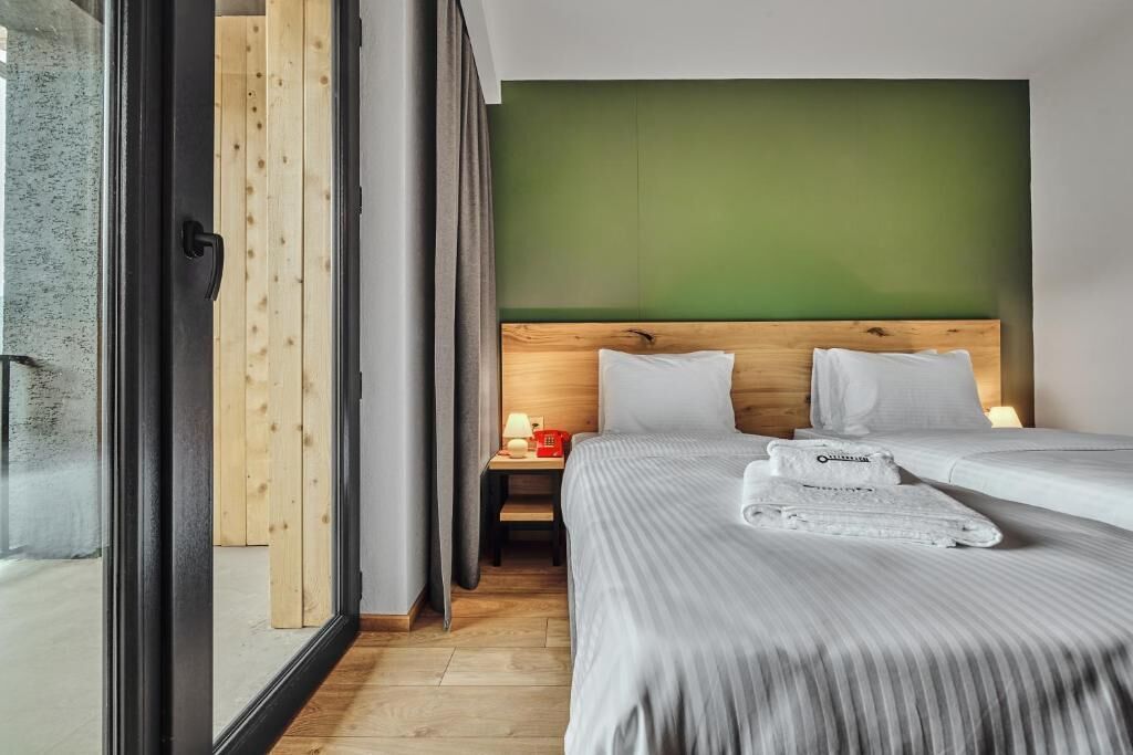 Een hotelkamer met twee bedden, een houten hoofdeinde, een groene accentmuur en een nachtkastje met een lamp.