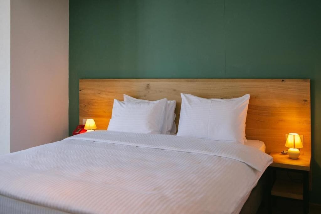 A neatly made bed with white linens and pillows, two bedside lamps, and a wooden headboard.