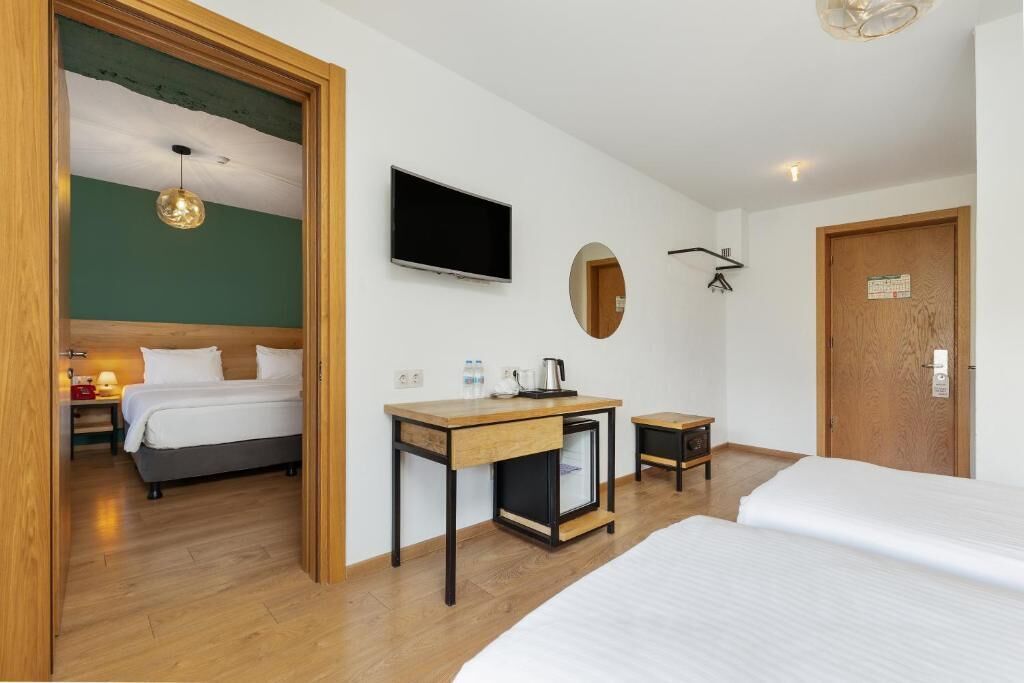 Quarto de hotel com uma cama, uma escrivaninha com computador, uma televisão e uma porta.