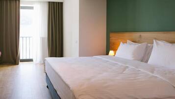 Ein Hotelzimmer mit einem großen Bett, einem Holzkopfende und Blick ins Freie durch ein Fenster mit Vorhängen.