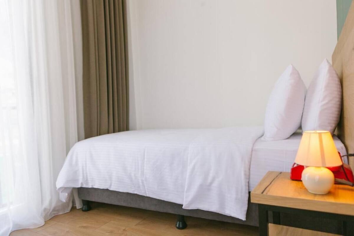A neatly made bed with white bedding, a bedside lamp, and two pillows on a wooden nightstand.