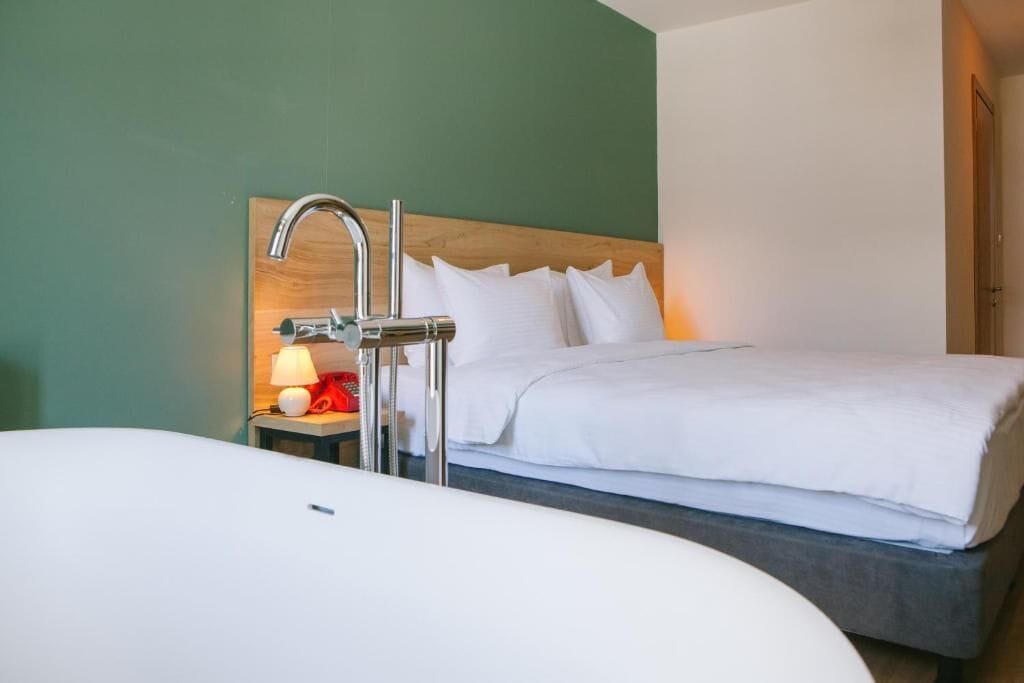 A hotel room with a bed, a nightstand with a lamp, and a large bathtub.