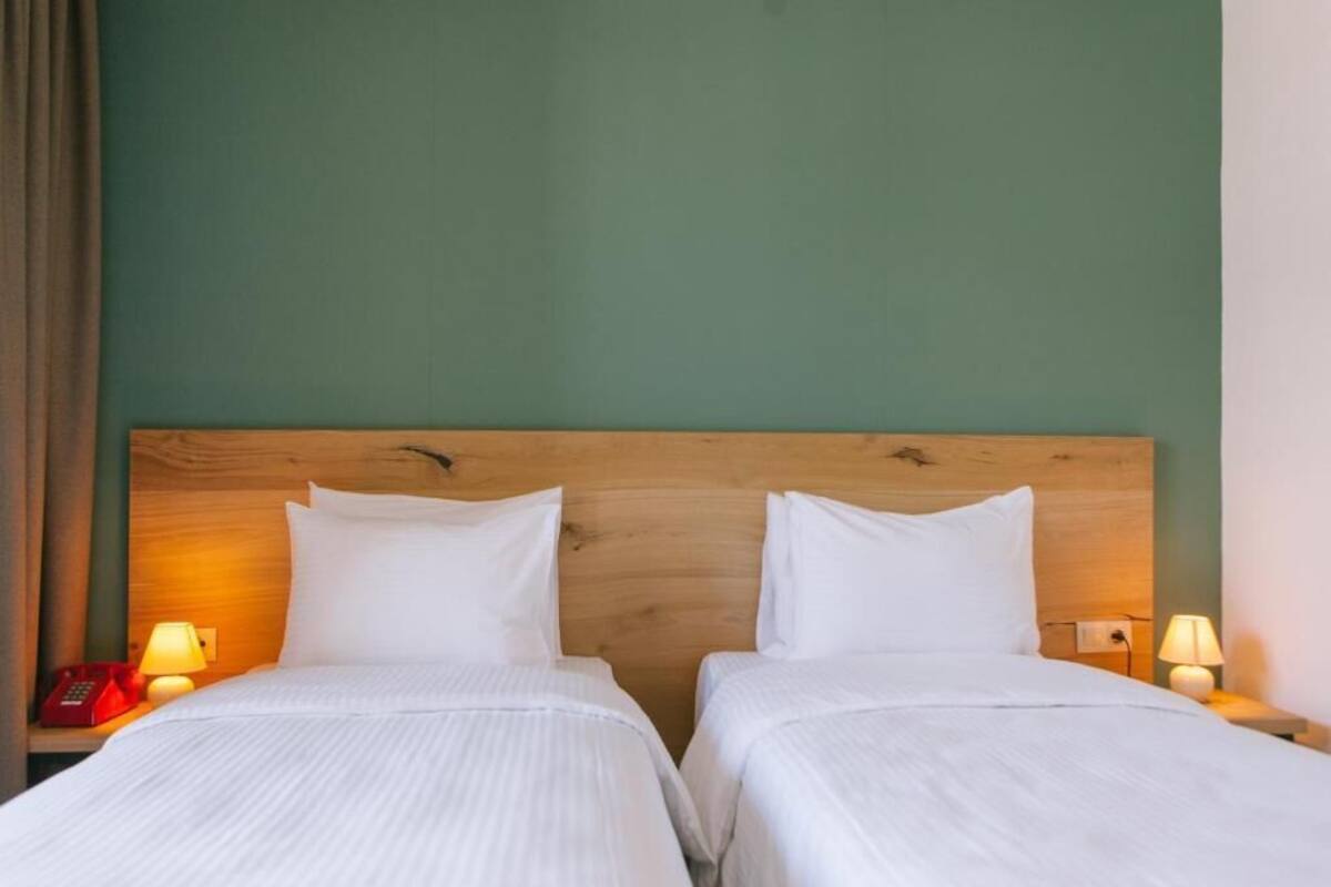 A hotel room with two single beds, wooden headboard, bedside lamps, and a green wall.