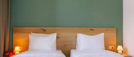 A hotel room with two single beds, wooden headboard, bedside lamps, and a green wall.