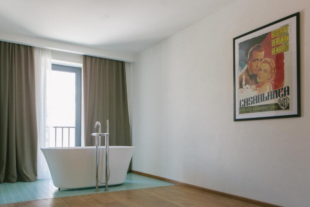 Un baño con una bañera independiente, cortinas color beige y un póster en la pared.