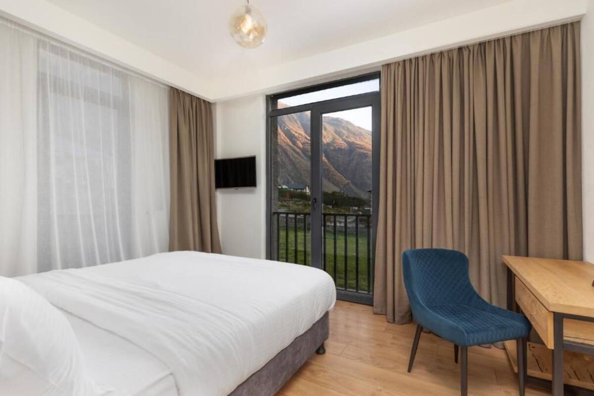 A hotel room with a bed, a desk, a chair, a TV, and a balcony with a mountain view.