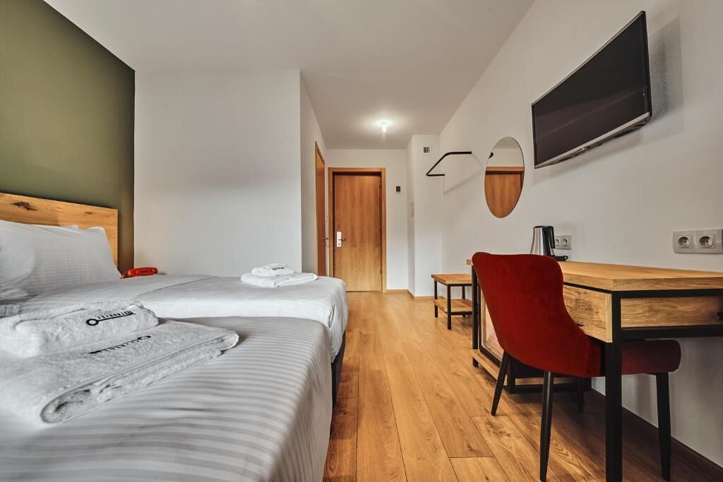 A hotel room with two beds, a desk, a chair, a TV, and a mirror.