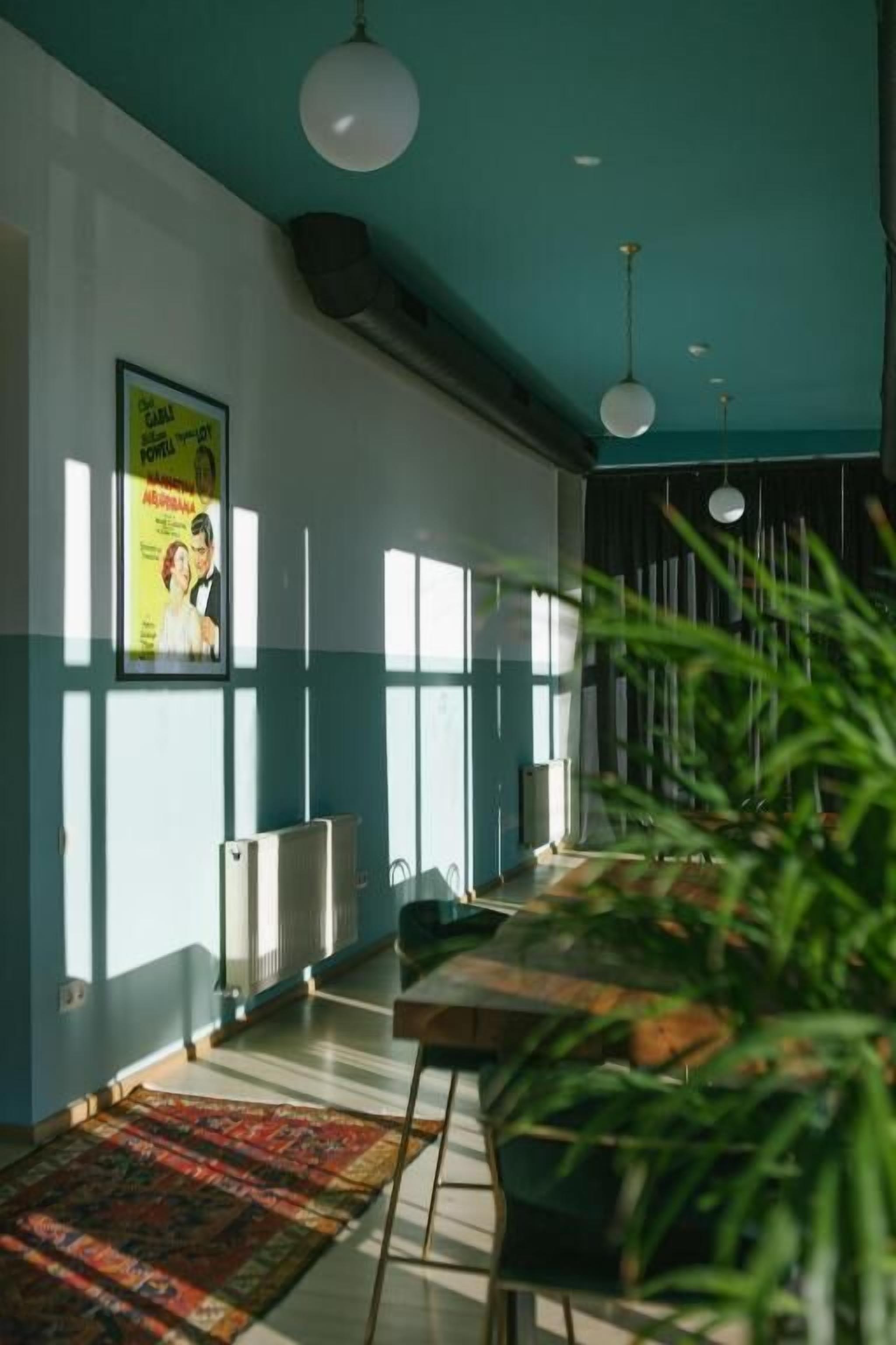 A modern room with a teal ceiling, large windows, a radiator, a patterned rug, and a poster on the wall.