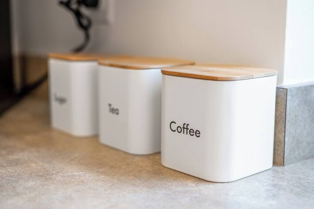 Tres recipientes blancos con tapas de madera etiquetados como 'Café', 'Té' y 'Jugo'.