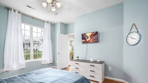 A bedroom with a bed, a dresser, a clock, and a window with curtains.