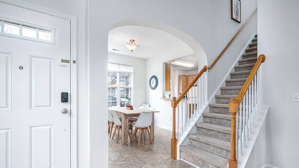A hallway with a white door, a staircase with wooden railings, and a dining area with a table and chairs.
