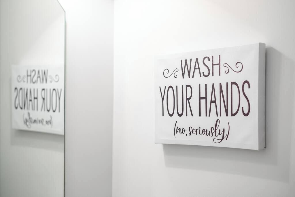 Una pared con un cartel que dice 'Lávate las manos (en serio)' en un baño.