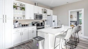 A modern kitchen with white cabinetry, stainless steel appliances, and a central island with bar stools.