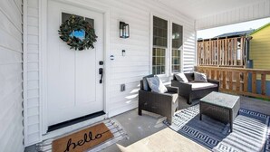 A porch with wicker furniture, a welcome mat, and a door with a wreath.