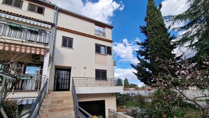 A multi-story building with a staircase leading to the entrance, a balcony, and a garden area with trees and flowering plants. - KATARINA B4 - Studio Apartment (Rovinj)