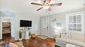 A living room with a ceiling fan, a television, a sofa, a coffee table, and a door leading to another room.
