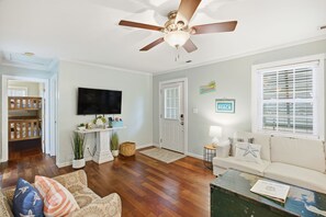 A living room with a ceiling fan, a television, a sofa, a coffee table, and a door leading to another room.