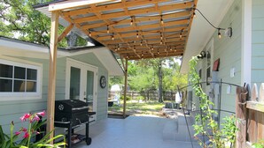 A covered patio area with a grill, a wooden pergola, and a garden with plants.
